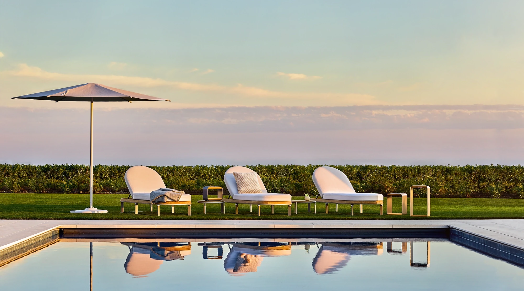 Outdoor chaise lounges and umbrella beside a reflecting pool at sunset