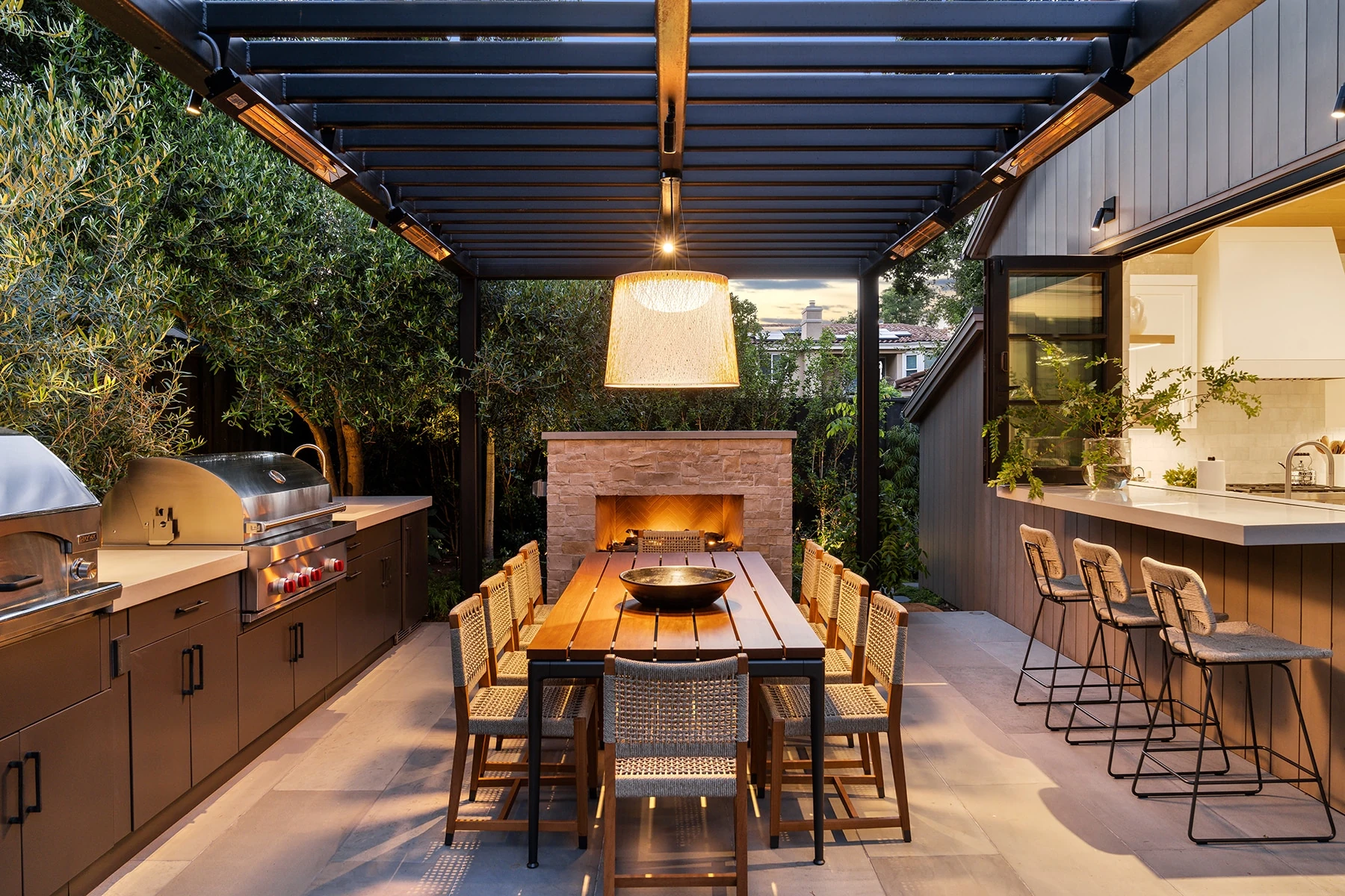 Covered outdoor dining area with dark cabinetry, grill, fireplace and integrated bar