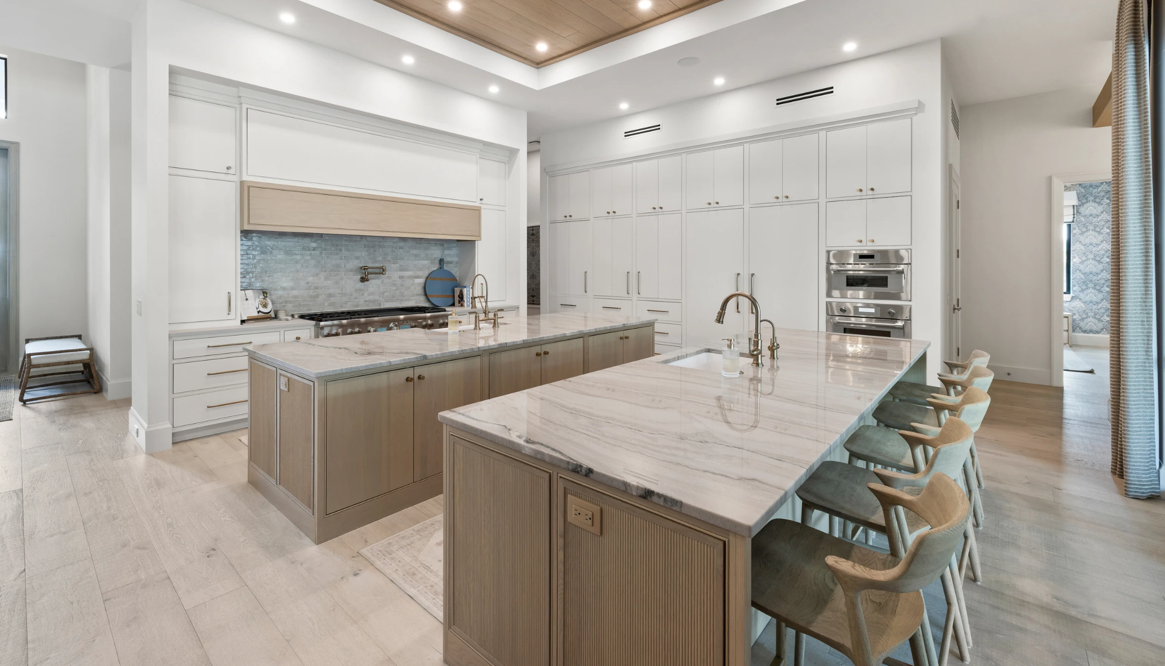 Pale wood kitchen cabinetry around two stone-topped islands