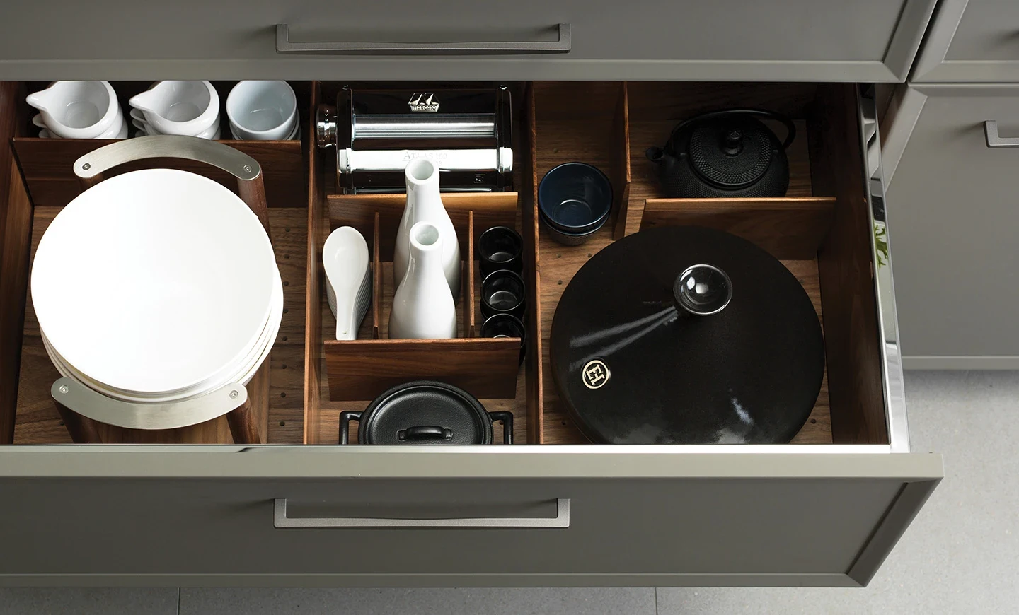 Slim metal cabinet pulls above an open drawer with fitted wood storage dividers