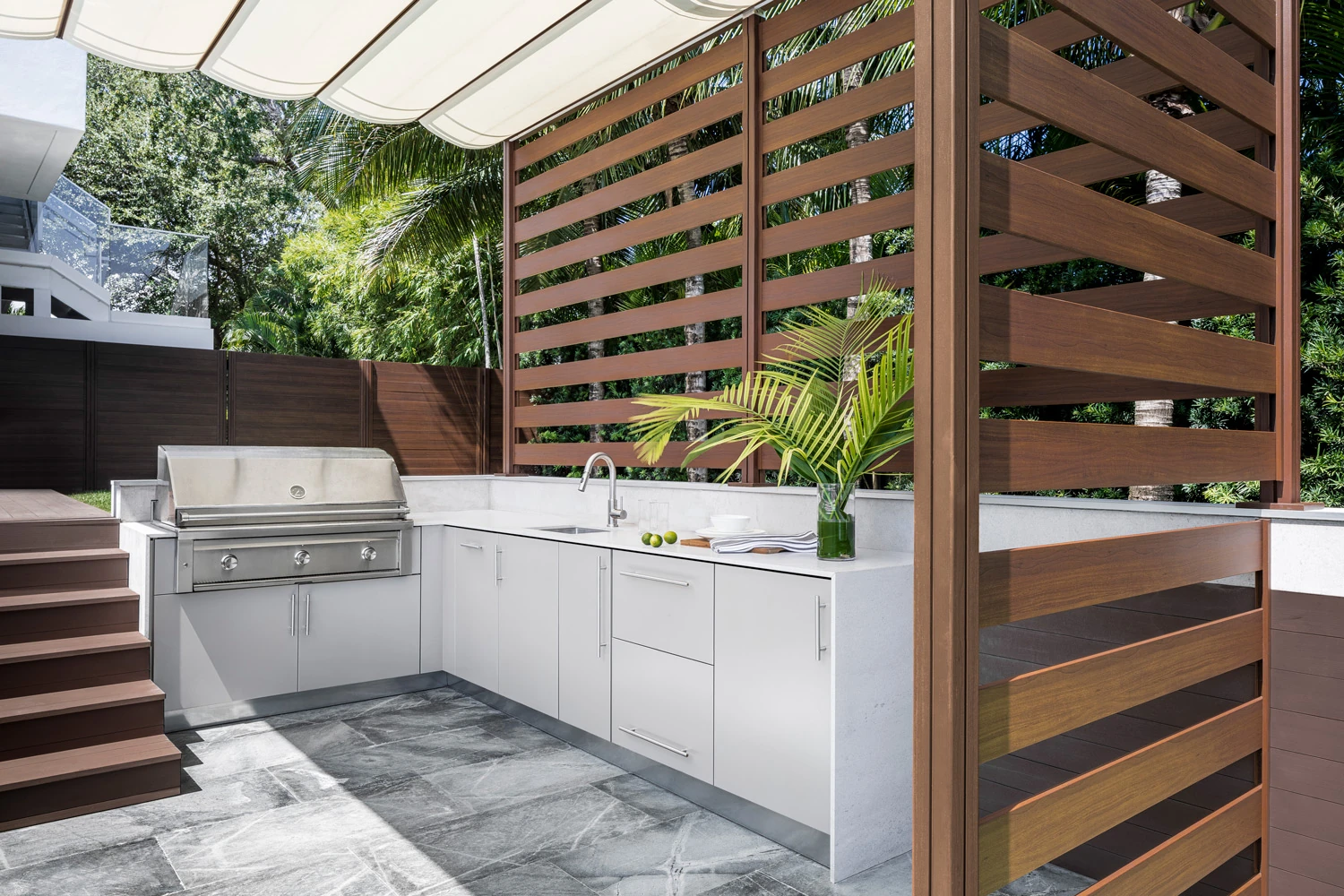 Pale outdoor cabinetry with an integrated grill, sink, and timber privacy screens